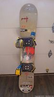 Full view of the snowboard from the top, showing logos, graphics, and bindings.