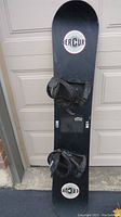 Full top view of black Mercury snowboard with attached black strap bindings, showing wear.