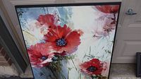 Full view of large floral painting featuring red flowers in black frame.