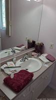 Wide view of bathroom sink area showing towels, bath mat, tissue box cover, waste bin, soap dish, votive holder and cup.