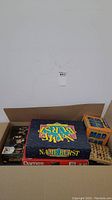 Open cardboard box showing assorted board games including "Name Burst", "Mad Gab", and "Dames"