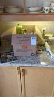 Box containing the two appliances and their parts on kitchen counter with cook book visible outside the box.