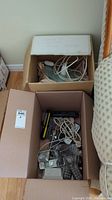 Box containing multiple Panasonic wireless cordless phones with cords and chargers, along with other electronic items.