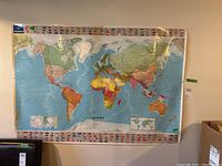 Laminated world map pinned to wall, with colorful countries and flags border.
