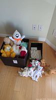 Photo of box and small open box containing various stuffed animals including a white ghost plush, yellow Garfield, clown, teddy bear, and multiple white dogs with holiday decorations.