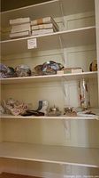 Shelves with various items including boxed silverware, ceramic teapots and bowls, and other collectibles.