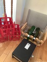 Wooden wine rack with four bottles, three metal shelves stacked behind, and three red plastic bottle baskets on the floor beside all items