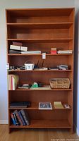 Front view of a tall solid wood bookshelf with seven fixed shelves and various items on the shelves illustrating size and structure.