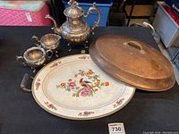 Photo showing the antique copper warming platter with colorful floral and bird motif insert, copper dome lid, and silver plated tea set consisting of teapot, creamer, and sugar bowl.