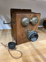 Front view showing wooden case, two metal bells, black mouthpiece and separate earpiece with cloth wiring.