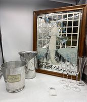 Photo showing framed Taylor champagne mirror art, two Moet & Chandon champagne buckets, and four champagne flutes on a white surface.