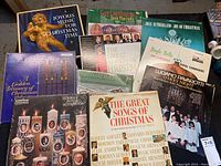 Multiple vintage Christmas LP albums arranged on a surface with visible festive themed covers including candles, angels, choirs, and titles.
