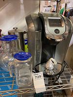 Keurig 2.0 coffee maker on metal shelf with glass carafes and French press nearby
