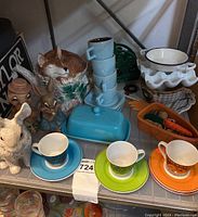 View of entire shelf showing fox teapot, stacked light blue espresso cups, rabbit figurines, butter dish, colorful espresso cup sets, metal chicken napkin holder, and ceramic egg holder.