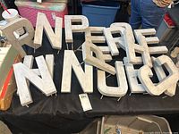 Lot of aluminum advertising letters arranged on a table, showing various letters and mounting pins.