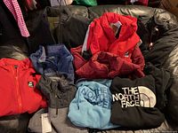 Various men's sweatshirts, jackets, and vests in different colors and brands arranged on a couch.