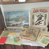Photo shows grouping of vintage paper ephemera arranged on a surface including coloring books, prints, and postcards.