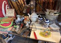 Overview of various vintage and decorative items on table including Votes for Women teapot, small animal figurines, ceramic condiment sets, floral tiles, and other kitchen and decorative pieces.