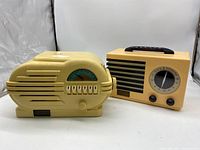 Yellow oval Crosley radio with six push buttons and blue dial in front, peach rectangular radio with large tuning dial and carry handle on top behind.