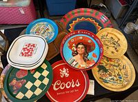 Image shows vintage serving trays stacked and arranged on a table including Corona, Coors beer metal trays and wooden souvenir trays