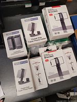 Lot view showing multiple boxed phone mounts including NOZEWOWA branded travel phone holders and desktop mobile phone brackets.