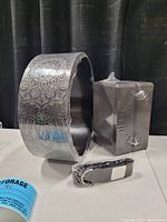 Photo showing the patterned yoga wheel, two sealed yoga blocks, and yoga strap laid out on a table with a dark fabric background.