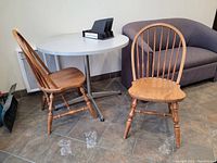 Two vintage wooden chairs with spindle backs and turned legs, situated in a room with tile flooring, a gray sofa, and a white table.