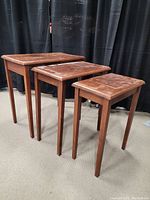 Photo showing three antique wooden nesting tables of different sizes arranged side by side with black curtain backdrop.