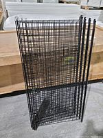 Five black metal wire grid panels stacked vertically, showing the thickness and mesh pattern of each piece.