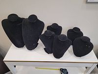 Seven black velvet necklace display busts arranged on a white table; 2 large, 3 medium, and 2 small busts visible with slight wear marks on velvet.