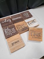 Top view of 8 wooden signs displaying inspirational or religious text such as joy, blessings, Child of God, faith, grace, and holiday-themed messages.