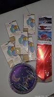 Five sealed packages of assorted quality balloons in color mix and giant red car gift bow, plus decorative plate.