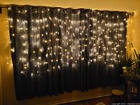 LED string curtain lights hanging over black drapes, emitting warm white light in a curtain pattern, showcasing the glow and coverage of the lights.
