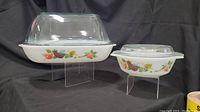 Two Pyrex bakeware dishes on clear display stands showing overall items with lids and pattern.