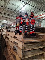 Three Halloween-themed weighted plush gnomes sitting on wooden pallets with dangling legs. One holds a black cat, one a broomstick, and one a pumpkin. All are brand new with tags.