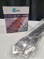 Box of Eden Products anti-slip stair tread covers sized 24 x 4 inches each, alongside two kitchen tongs in sealed plastic packaging.
