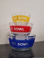 Three vintage glass nesting bowls stacked, showing yellow 1 QT bowl on top, red 1.5 QT bowl in middle, and blue 2.5 QT bowl on bottom, all with bold white text and primary colored bands.