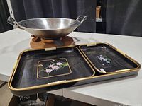 Image of large metal cooking wok on wooden spinning pedestal with two black trays in front