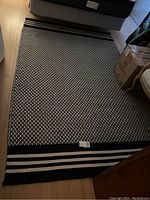 Full view of the black and white patterned area rug placed on hardwood floor with striped ends visible.