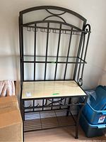 Front view of the metal baker's rack showing wood surface countertop, stemware storage hooks, and wine rack structure.