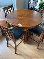 Round wooden bar height dining table with four matching chairs, showing wear and cracks in vinyl seats.