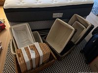 Wide shot of six assorted rectangular storage baskets nested and arranged on patterned carpet in front of a mattress.