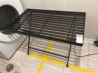 Image of black metal folding table with slatted top next to a dryer, showing legs and surface from side angle.