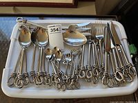 Full view of the entire cutlery set laid out on a white tray showing spoons, forks, and serving utensils with rope and knot design handles.