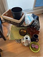 Photo showing variety of home decor items including basket, planter, vase, stein, placemats, candles and small decorative items.