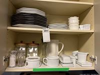 Contents of shelf holding stacked plates, ramekins, glass canisters, salt and pepper shakers, butter dish and creamer pitcher.