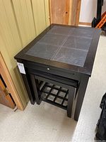 Side angle of the wooden end table with leather-like top and matching stool pushed underneath.
