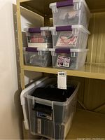 Five plastic storage totes on shelving filled with assorted CDs and DVDs with purple handles visible.