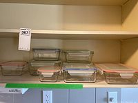 Front view of multiple glass food storage containers on a shelf showing variety of sizes and colored lids