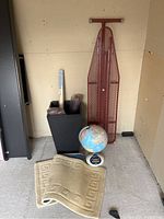 Full lot showing ironing board, globe, planter with brushes and folded rug.